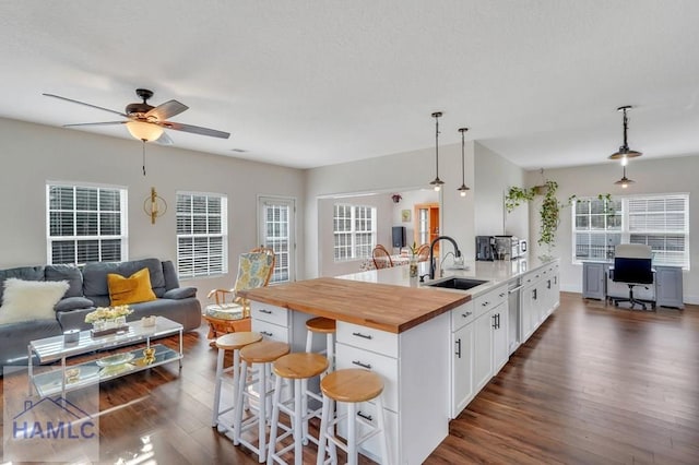 kitchen with white cabinetry, sink, wood counters, pendant lighting, and a kitchen island with sink