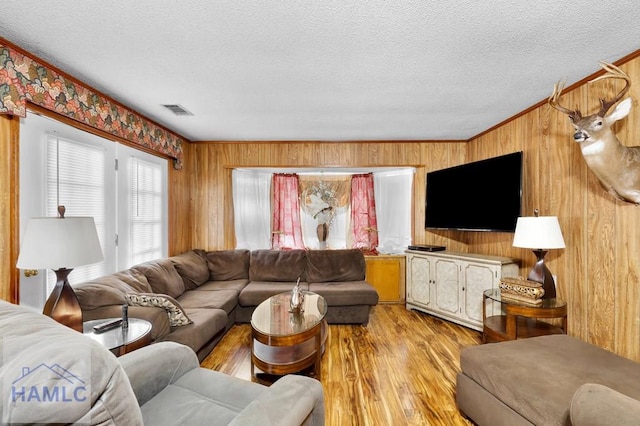 living room featuring a textured ceiling, light wood-type flooring, ornamental molding, and wooden walls