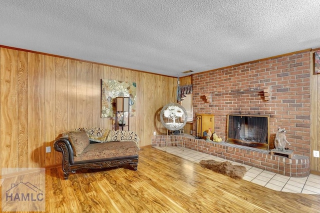 living room with a brick fireplace, ornamental molding, a textured ceiling, light hardwood / wood-style floors, and wood walls