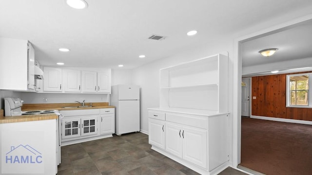 kitchen with butcher block countertops, wood walls, white cabinetry, sink, and white appliances