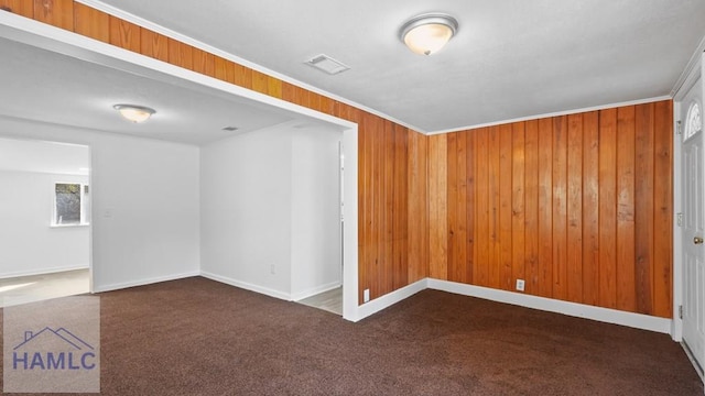 unfurnished room with dark colored carpet, crown molding, and wood walls