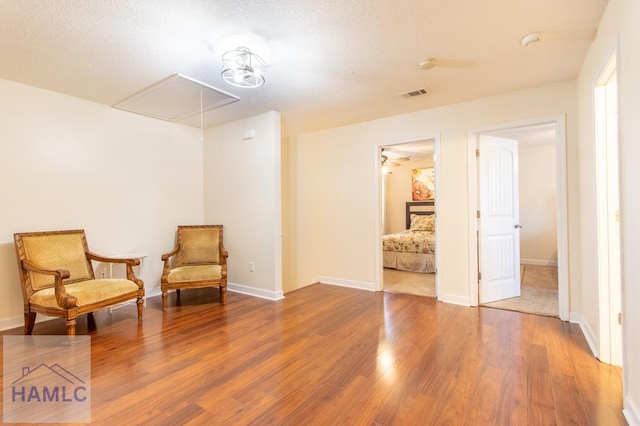 sitting room featuring baseboards, attic access, visible vents, and wood finished floors