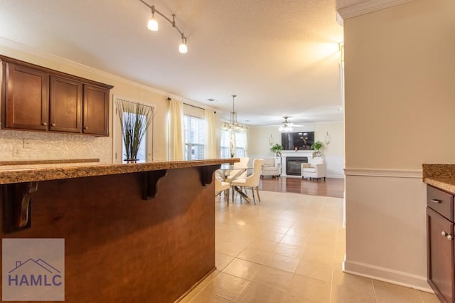 kitchen with a breakfast bar, open floor plan, ornamental molding, decorative backsplash, and a glass covered fireplace