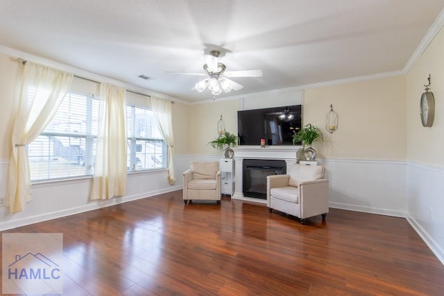 living area with a ceiling fan, visible vents, dark wood-style floors, a glass covered fireplace, and crown molding