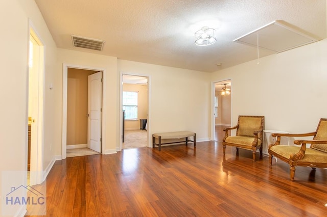 sitting room featuring visible vents, attic access, a textured ceiling, wood finished floors, and baseboards