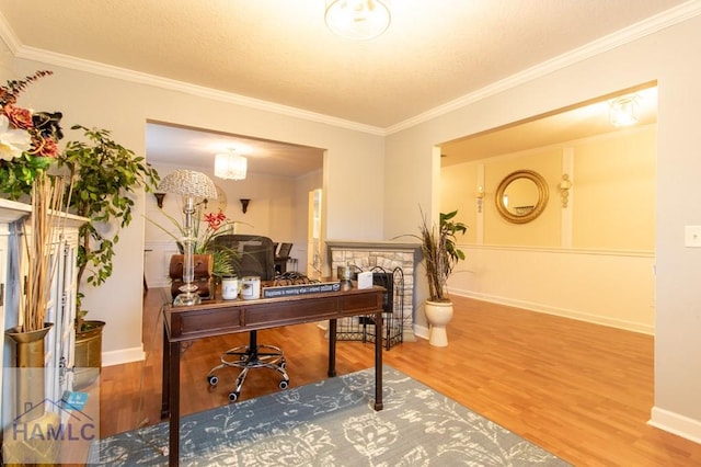 home office with ornamental molding, wood finished floors, and a stone fireplace