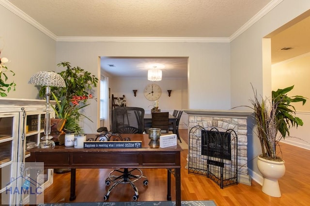 home office with a textured ceiling, ornamental molding, a fireplace with raised hearth, and wood finished floors