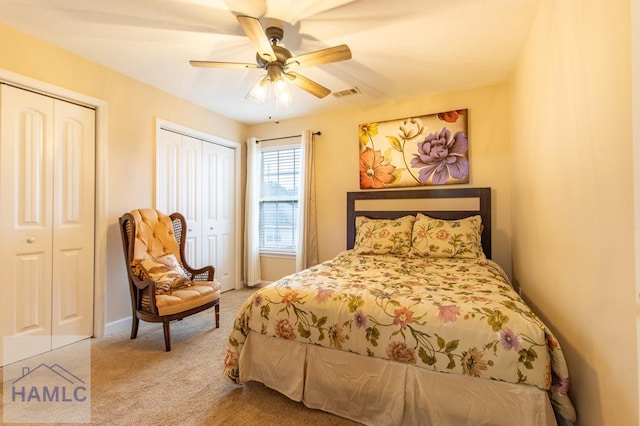 bedroom featuring multiple closets, light colored carpet, visible vents, and ceiling fan