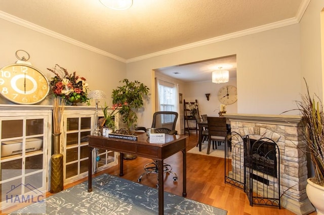 office space with a textured ceiling, a stone fireplace, a notable chandelier, wood finished floors, and crown molding