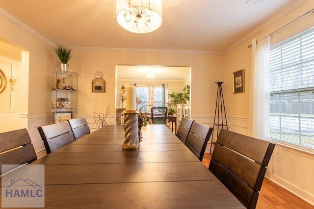 dining space with an inviting chandelier, light wood-style flooring, ornamental molding, and wainscoting