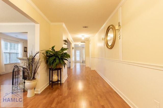 hall featuring baseboards, crown molding, visible vents, and wood finished floors