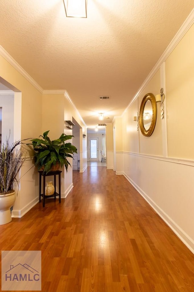 hallway with a textured ceiling, wood finished floors, visible vents, and crown molding