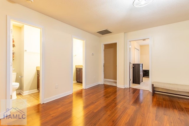 unfurnished bedroom featuring baseboards, visible vents, connected bathroom, and wood finished floors