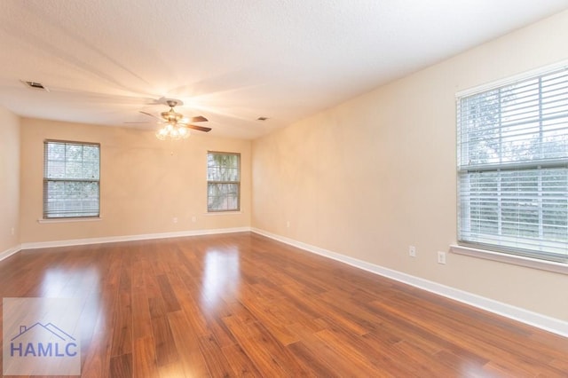 empty room featuring a ceiling fan, visible vents, baseboards, and wood finished floors