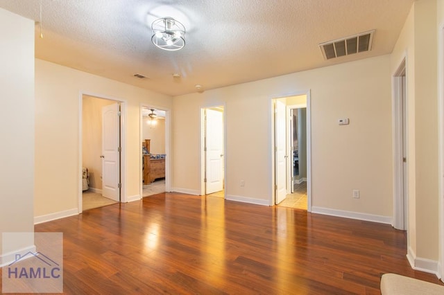 unfurnished bedroom featuring a textured ceiling, connected bathroom, wood finished floors, visible vents, and baseboards