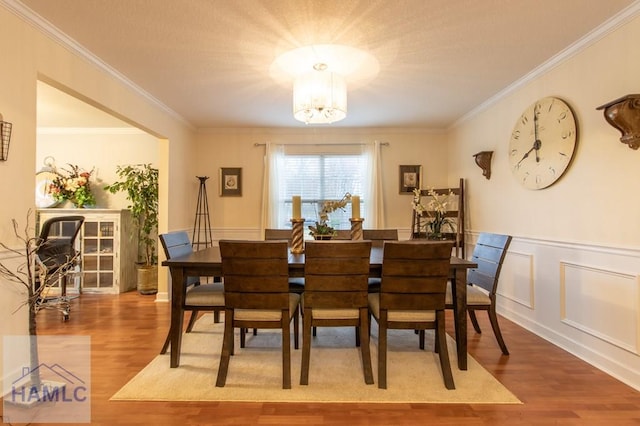 dining room featuring a wainscoted wall, wood finished floors, an inviting chandelier, crown molding, and a decorative wall