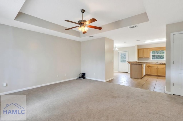 unfurnished living room featuring light carpet, sink, a raised ceiling, and ceiling fan