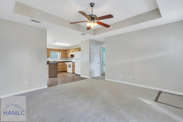 unfurnished living room with ceiling fan, a tray ceiling, and light carpet