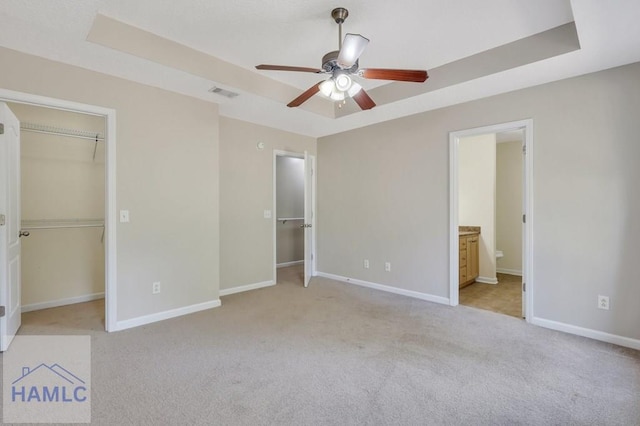 unfurnished bedroom with light colored carpet, connected bathroom, a spacious closet, and a raised ceiling