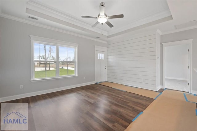 empty room with a ceiling fan, a tray ceiling, wood finished floors, and visible vents