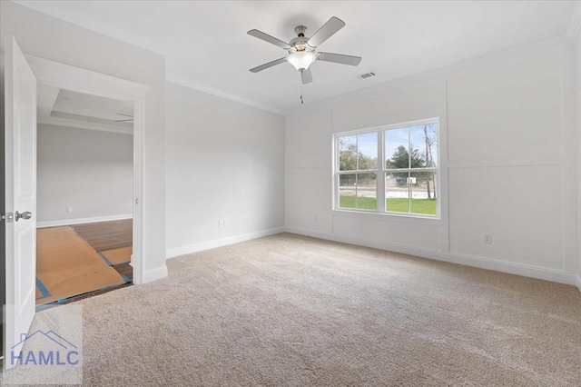 carpeted spare room featuring visible vents, baseboards, crown molding, and a ceiling fan