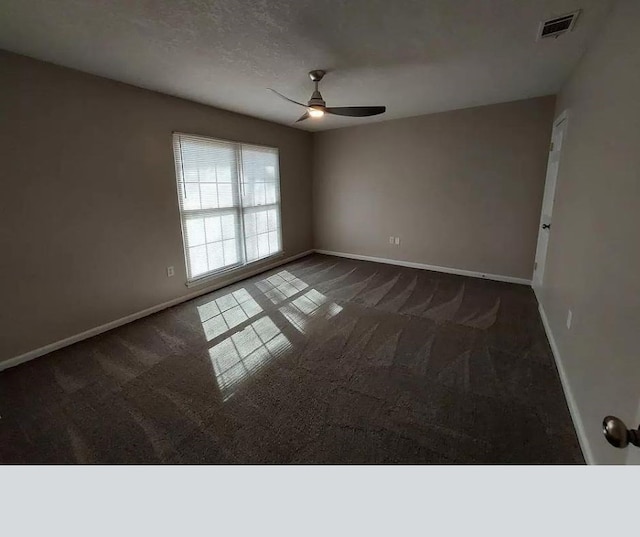 spare room with ceiling fan, dark carpet, and a textured ceiling