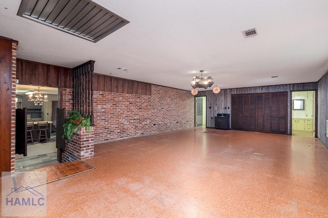 401E Smith St, Claxton, GA 30417 - unfurnished living room with a chandelier, brick wall, wooden walls, and speckle patterned floor
