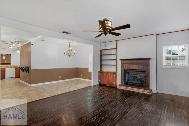 unfurnished living room featuring light wood finished floors, a fireplace, visible vents, and ceiling fan with notable chandelier