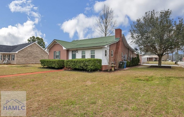 view of front of house featuring a front yard, a chimney, metal roof, and brick siding