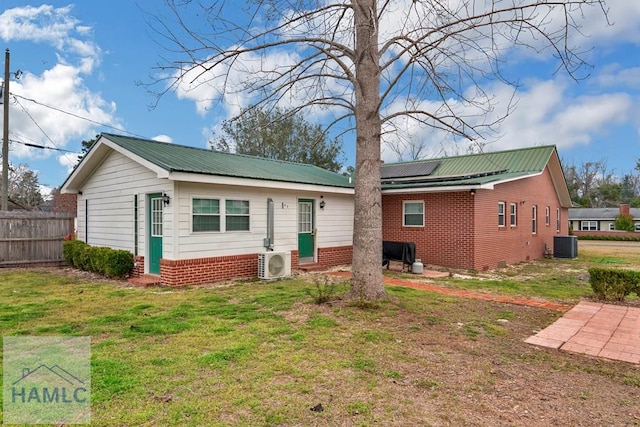 back of property featuring central AC, fence, a yard, roof mounted solar panels, and ac unit