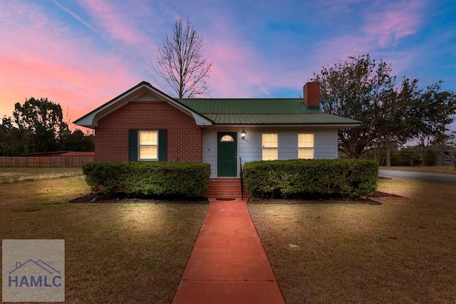 view of front of property with metal roof, a chimney, a front lawn, and brick siding