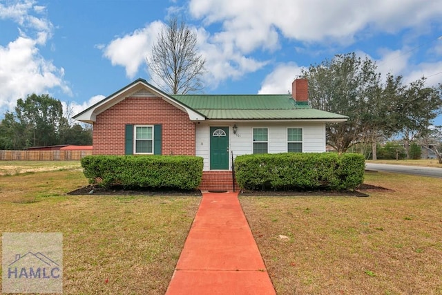 view of front of property featuring a chimney, brick siding, a front yard, and metal roof