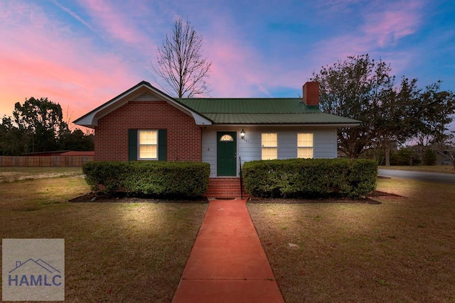 view of front of house featuring brick siding, a chimney, a front lawn, and metal roof