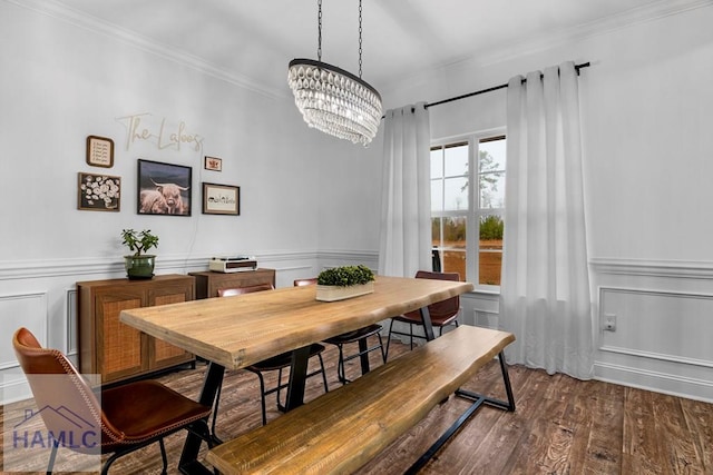 dining area featuring dark wood-style floors, a wainscoted wall, ornamental molding, a decorative wall, and a notable chandelier