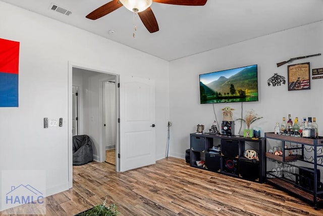 living room featuring a ceiling fan, visible vents, baseboards, and wood finished floors