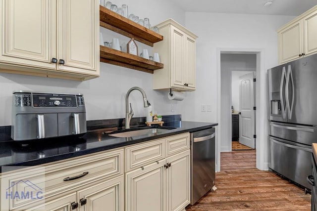 kitchen with cream cabinets, appliances with stainless steel finishes, open shelves, and a sink