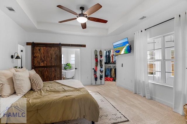 bedroom with light carpet, a barn door, visible vents, a raised ceiling, and a spacious closet