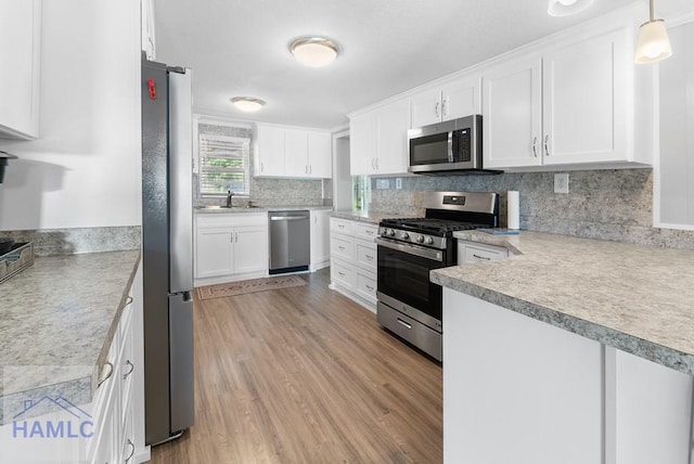 kitchen with appliances with stainless steel finishes, light wood-type flooring, sink, decorative light fixtures, and white cabinets