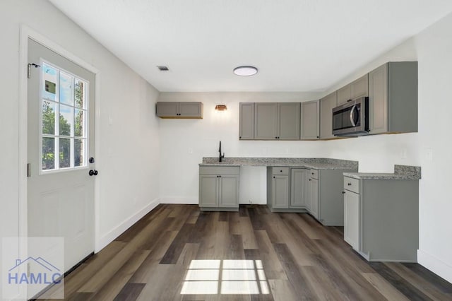 kitchen with dark wood-style flooring, visible vents, gray cabinetry, a sink, and stainless steel microwave