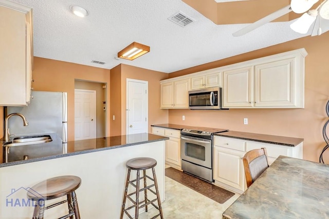 kitchen featuring appliances with stainless steel finishes, a kitchen breakfast bar, a textured ceiling, ceiling fan, and sink