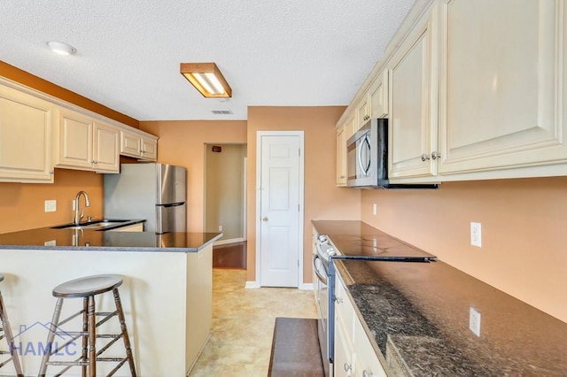 kitchen featuring a kitchen bar, sink, stainless steel appliances, and a textured ceiling