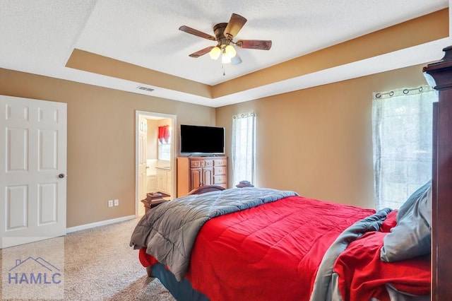 carpeted bedroom with a textured ceiling, connected bathroom, a raised ceiling, and ceiling fan