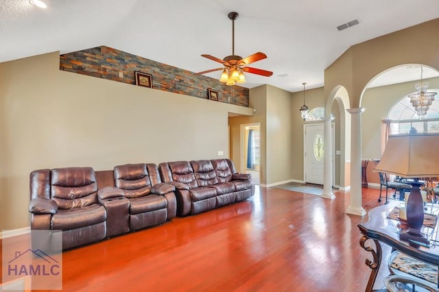 living room with ornate columns, ceiling fan with notable chandelier, wood-type flooring, and vaulted ceiling