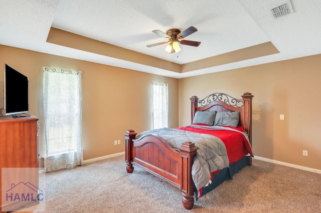 carpeted bedroom featuring ceiling fan, a raised ceiling, a textured ceiling, and multiple windows