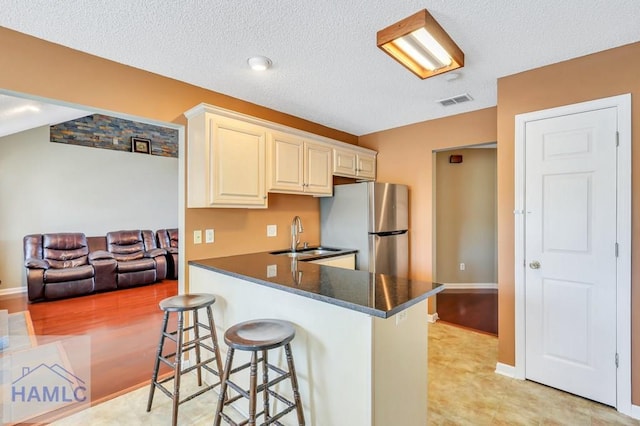 kitchen featuring kitchen peninsula, stainless steel fridge, a kitchen breakfast bar, a textured ceiling, and sink