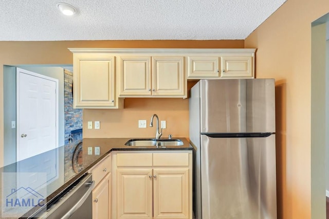 kitchen with appliances with stainless steel finishes, dark stone counters, a textured ceiling, sink, and cream cabinets