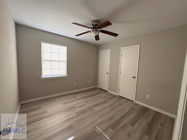 unfurnished bedroom with ceiling fan, baseboards, light wood-type flooring, and a textured ceiling