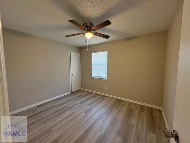 empty room featuring ceiling fan, wood finished floors, baseboards, and a textured ceiling