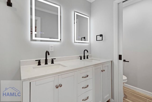 full bathroom with toilet, double vanity, wood finished floors, baseboards, and crown molding