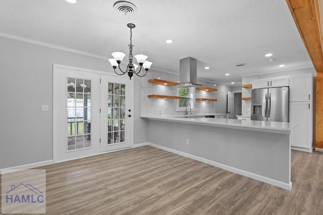 kitchen featuring stainless steel refrigerator with ice dispenser, open shelves, island range hood, light countertops, and a textured ceiling